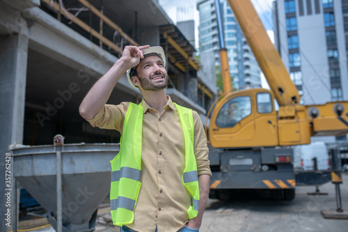 Bild auf Leinwand Building worker in helmet and yellow vest touching his helmet with his hand, loo