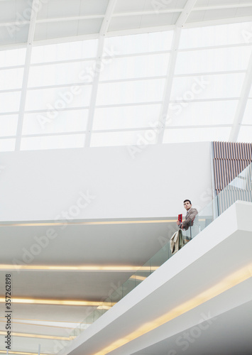 Businessman standing at glass balcony railing in modern building