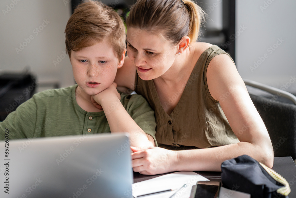 Mother homeschooling her son and using laptop at home Mother homeschooling her son and using laptop at home