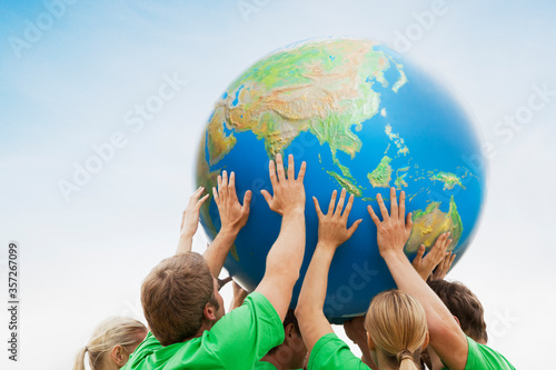 Fotografie Team in green t-shirts lifting globe overhead