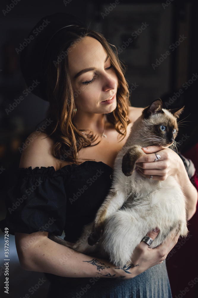 Lovely woman playing with Siamese cat at home. Friendship between humans and animals