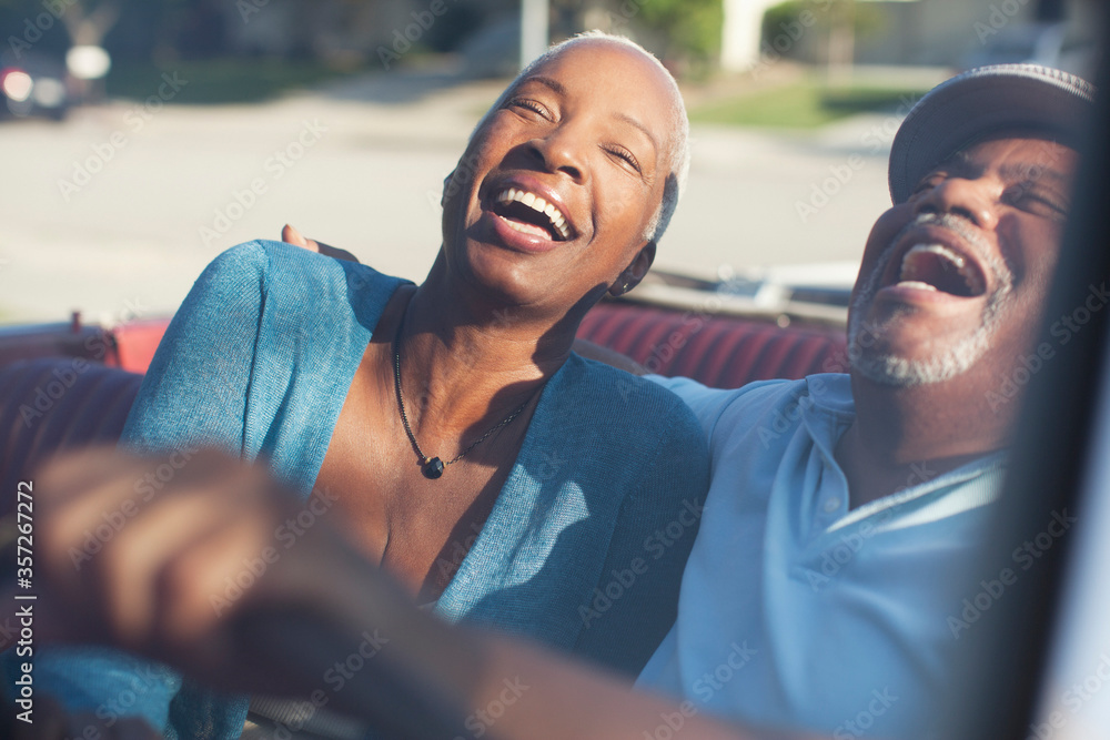 Older couple laughing in convertible - obrazy, fototapety, plakaty 