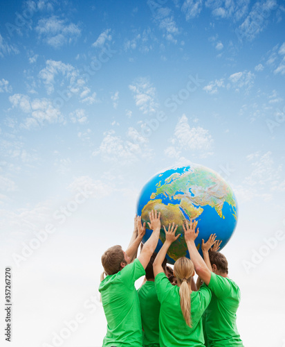 Team in green t-shirts lifting globe overhead