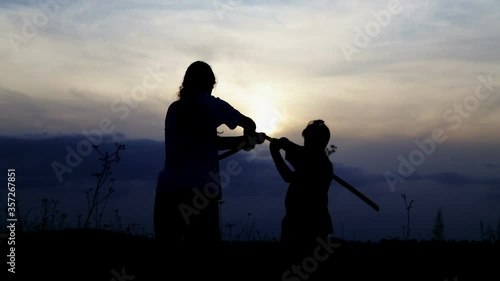 Teenage boys fencing with samurai training swords. Silhouette of exercising children in a field with swords.