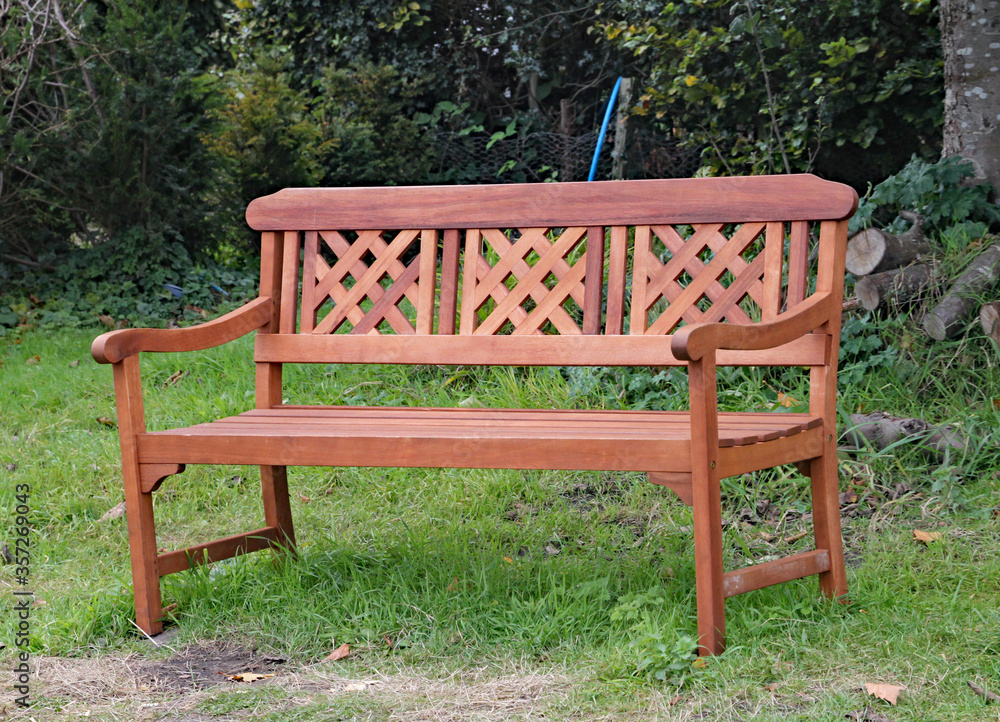 Ornate park bench on the grass in front of some lush woodland Ornate park bench on the grass in front of some lush woodland