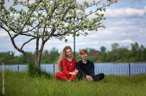 A young man and a girl sit under a blooming Apple tree