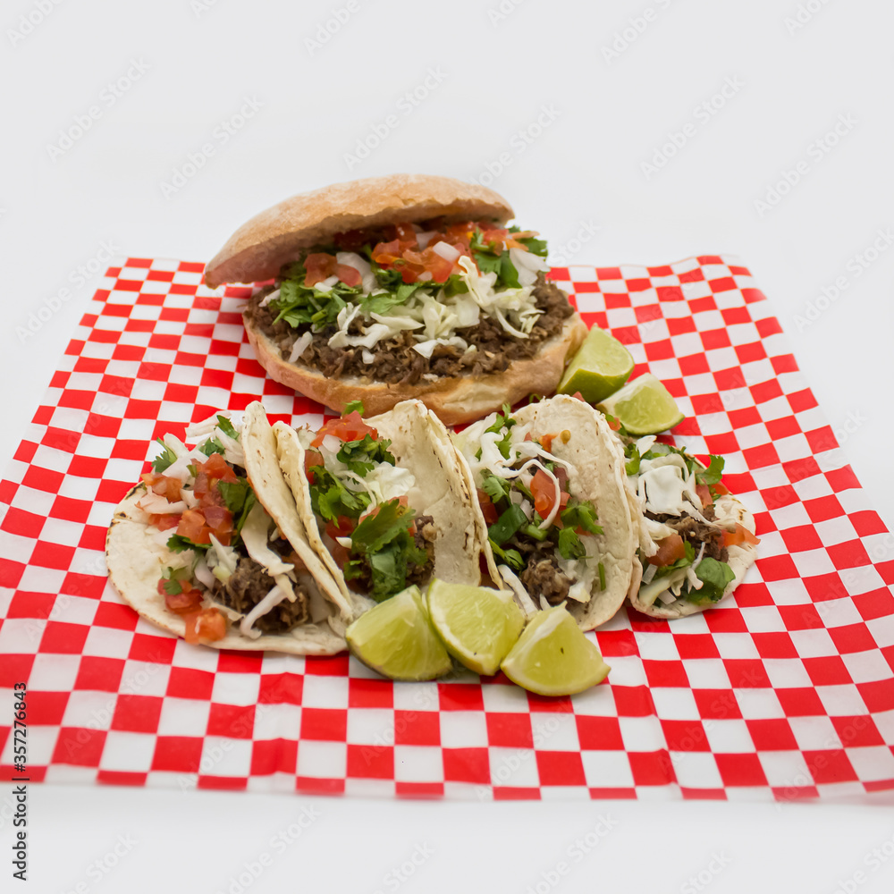 Tacos y tortas de barbacoa sobre mantel de cuadros rojos y fondo blanco