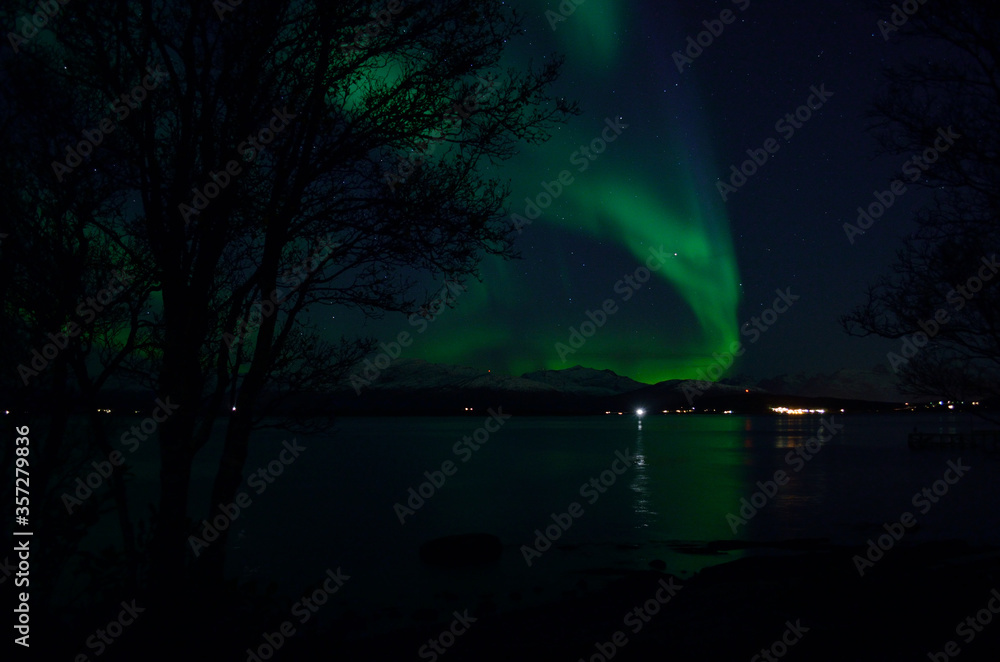 vibrant aurora borealis over fjord and mountain reflecting on fjord surface at night
