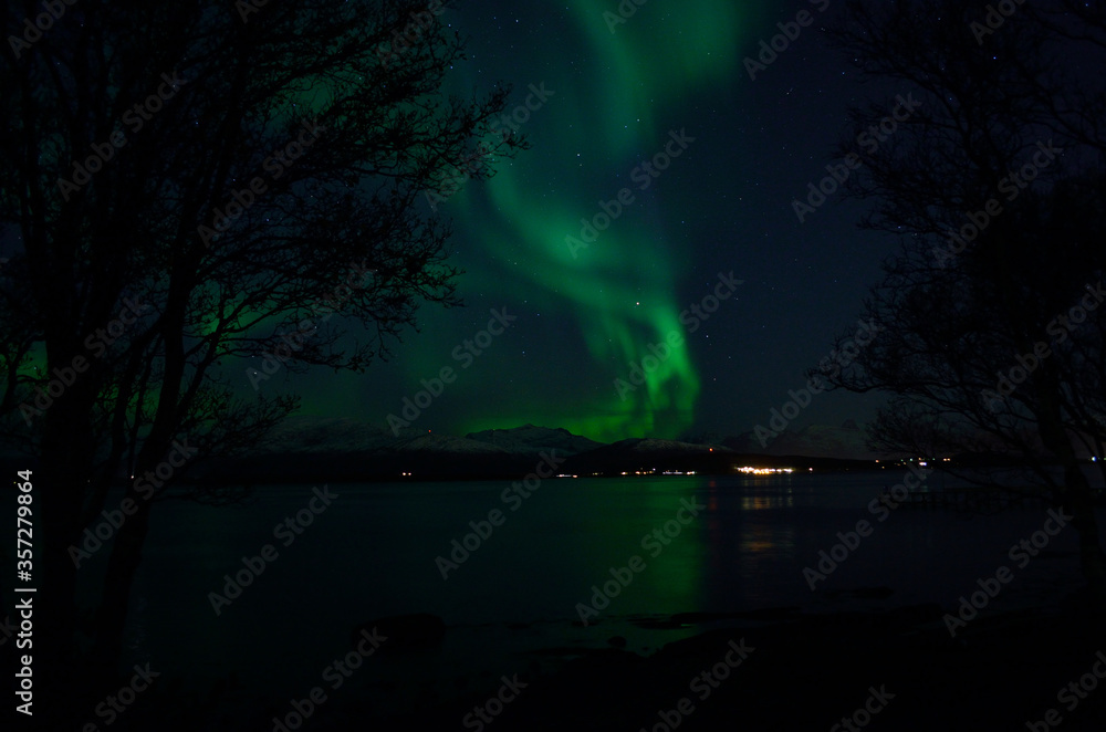 vibrant aurora borealis over fjord and mountain refleting in sea surface