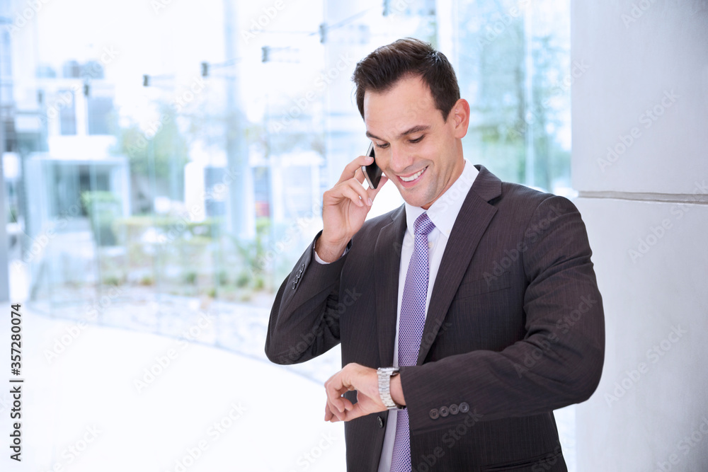 Smiling businessman talking on cell phone and looking at wristwatch Smiling businessman talking on cell phone and looking at wristwatch