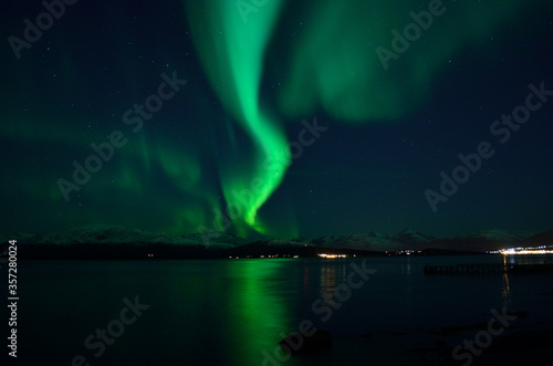 incredible strong aurora borealis over fjord and snowy mountain