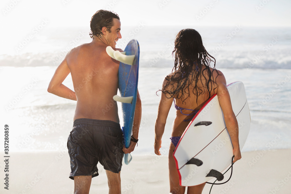 Couple walking with surfboards on beach Couple walking with surfboards on beach