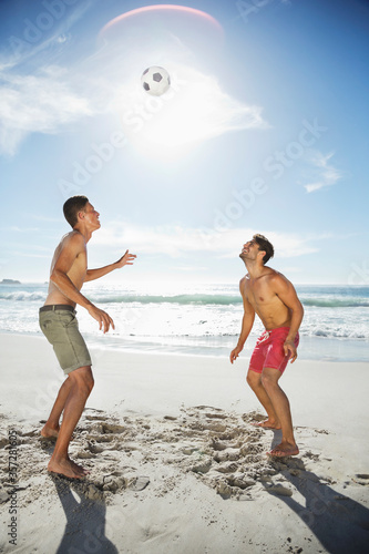 Men in swim trunks heading soccer ball on beach