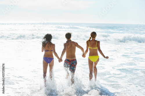 Friends holding hands and running into ocean
