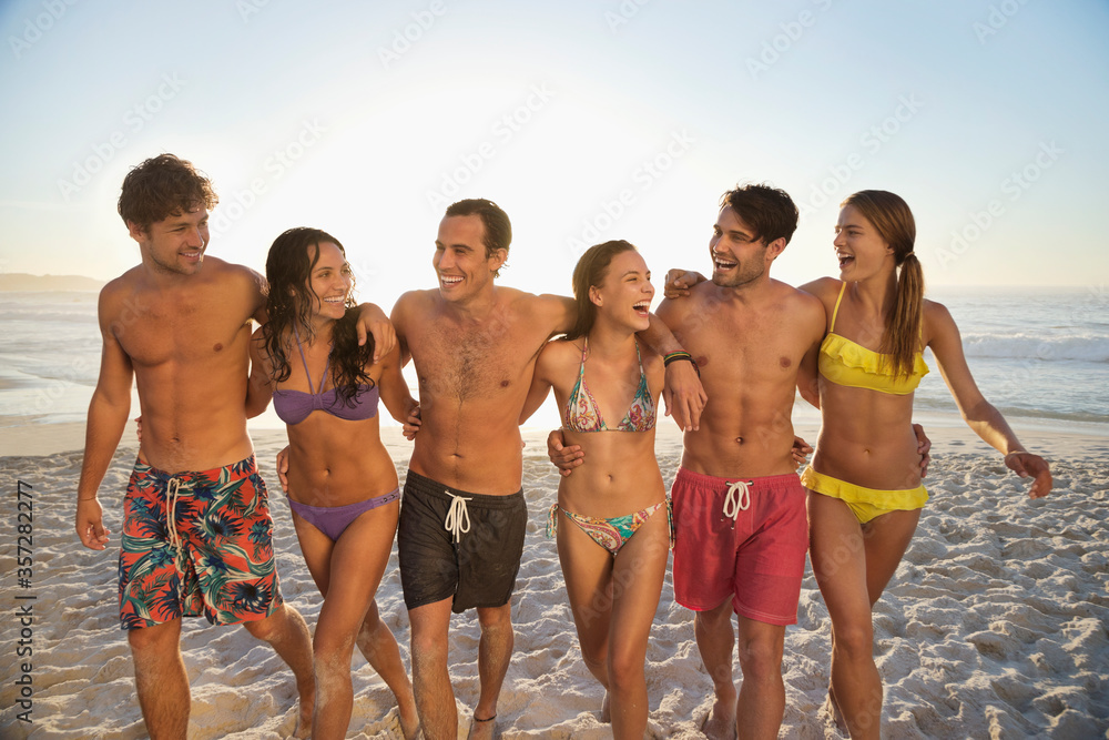 Happy friends in bikinis and swim trunks walking on beach Happy friends in bikinis and swim trunks walking on beach