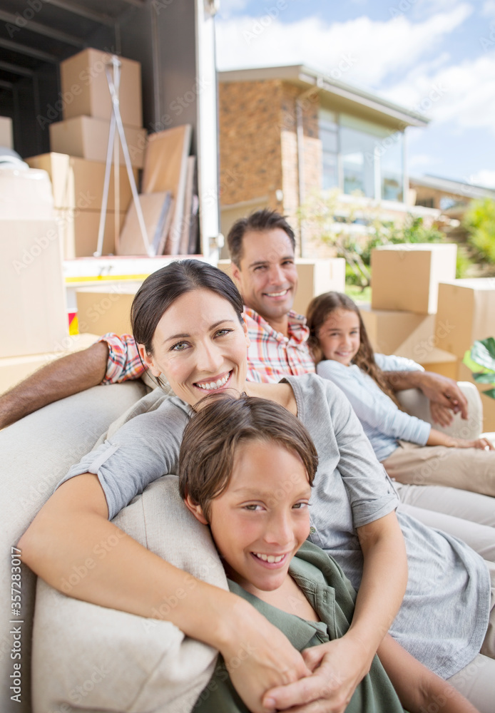 Family sitting on sofa near moving van in driveway Family sitting on sofa near moving van in driveway
