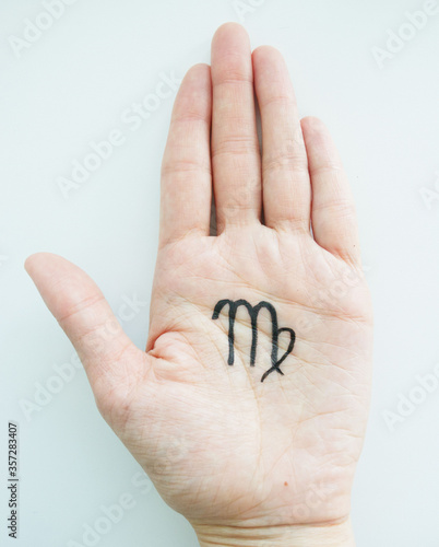 On the palm of a young girl is a top view, with a black felt-tip pen the zodiac sign Virgo is drawn, on a light background. Features, characteristics of the sign of Virgo in the palm of your hand, 