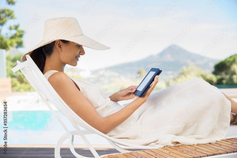 Woman using digital tablet on lounge chair at poolside