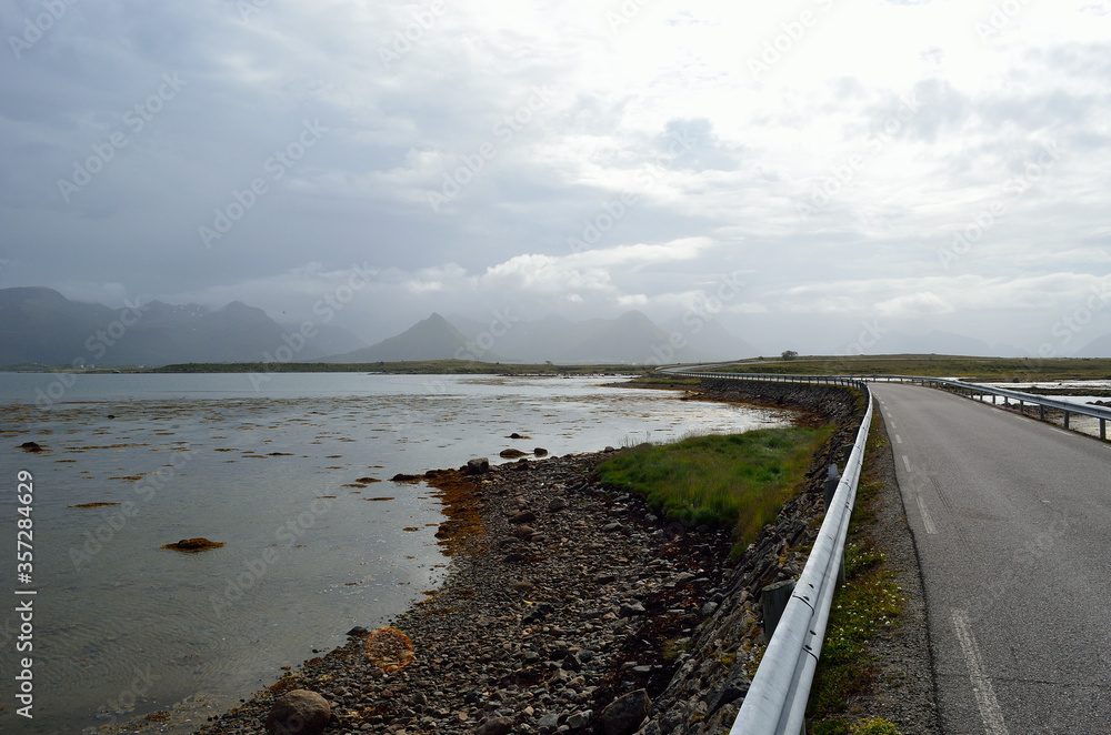 long road through flat landscape with mountain in background and ocean on sides long road through flat landscape with mountain in background and ocean on sides