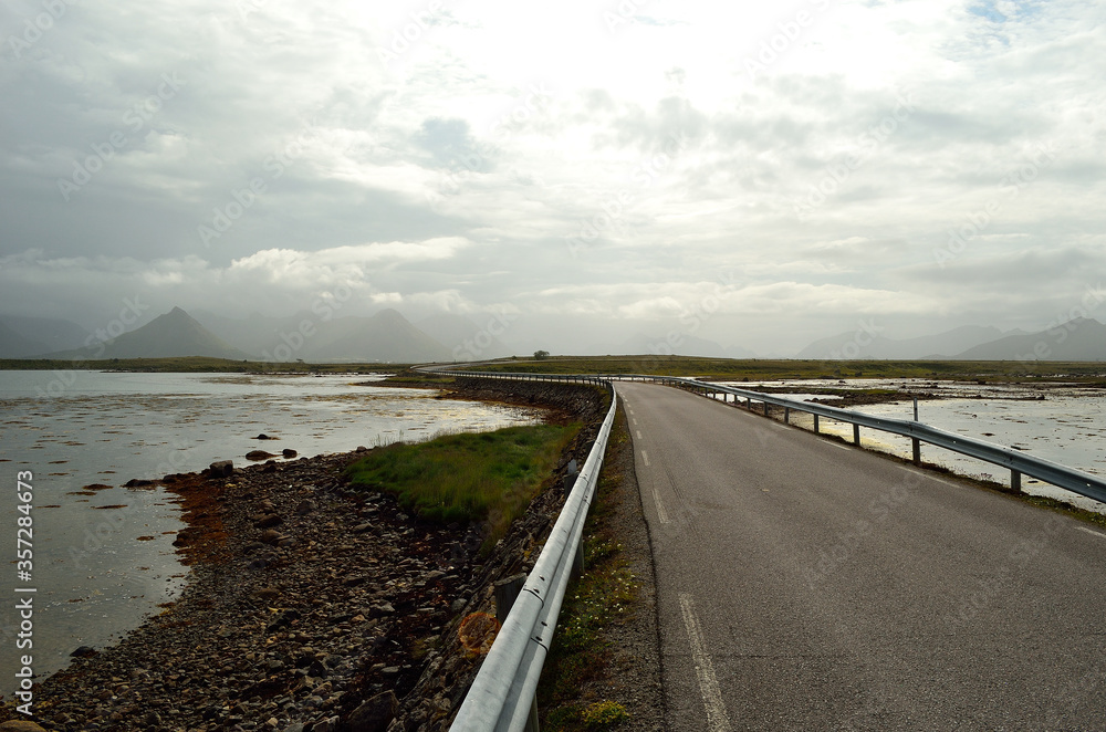 long road through flat landscape with mountain in background and ocean on sides long road through flat landscape with mountain in background and ocean on sides