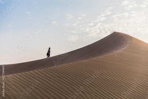 woman walking to the top of a dune in the desert