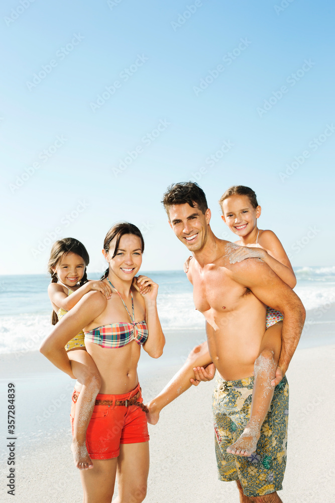 Parents carrying daughters piggyback on beach Parents carrying daughters piggyback on beach