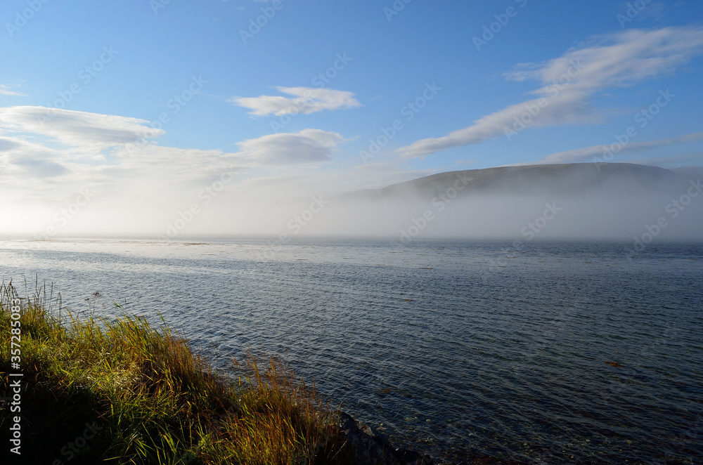 sea fog floating over blue fjord on blue sunny autumn day