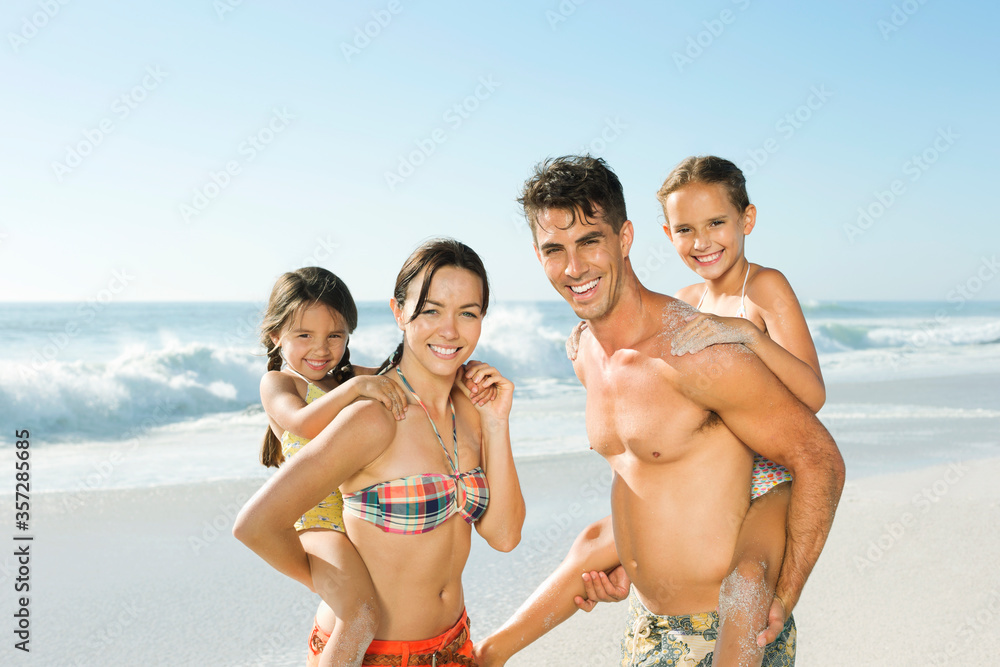 Parents carrying daughters piggyback on beach Parents carrying daughters piggyback on beach