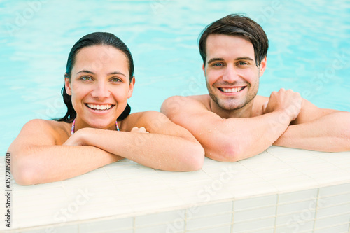 Portrait of smiling couple leaning at edge of swimming pool