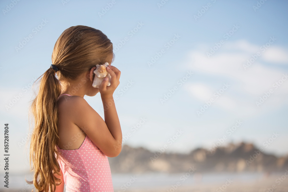 Girl listening to seashell on beach