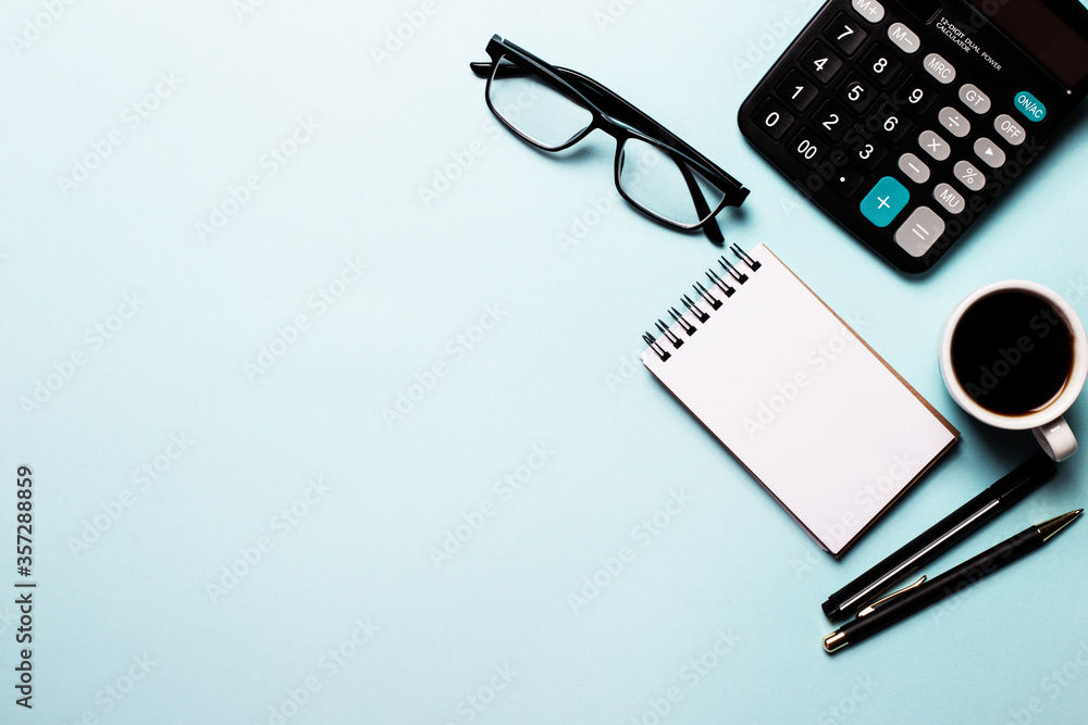 On a blue background are a pen, notebook, calculator, glasses and a cup of coffee. Top view, place for an inscription, business concept On a blue background are a pen, notebook, calculator, glasses and a cup of coffee. Top view, place for an inscription, business concept