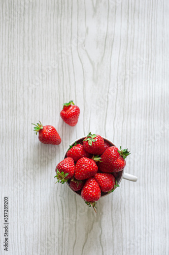 Strawberries in a cup on a light wooden background. View from above.