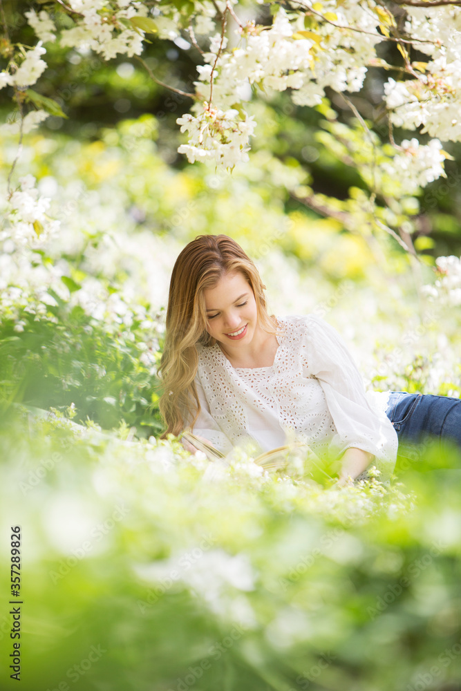 Woman reading book in grass under tree with white blossoms Woman reading book in grass under tree with white blossoms