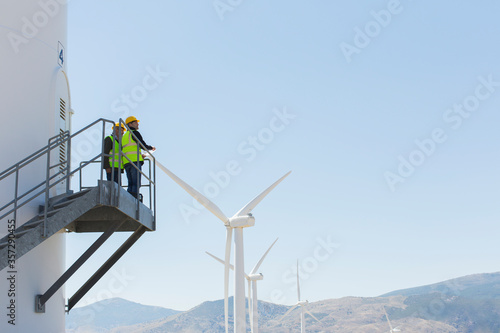 Workers standing on wind turbine in rural landscape photo