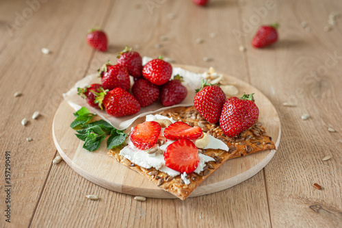 A healthy light breakfast with strawberries  cream cheese  nuts and seeds. On a wooden background in warm tones.