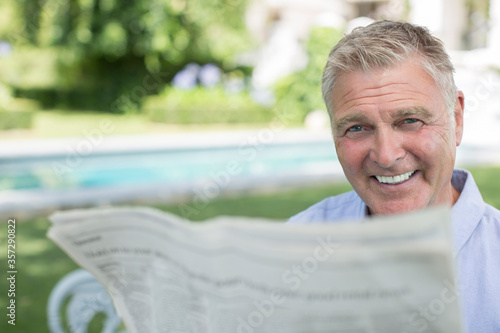 Senior man reading newspaper at poolside