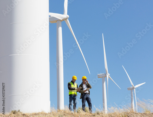 Workers talking by wind turbines in rural landscape photo