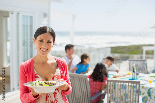 Woman holding salad bowl on sunny patio overlooking ocean