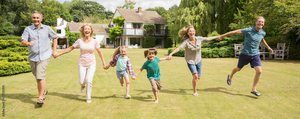 Multi-generation family holding hands and running in grass Multi-generation family holding hands and running in grass