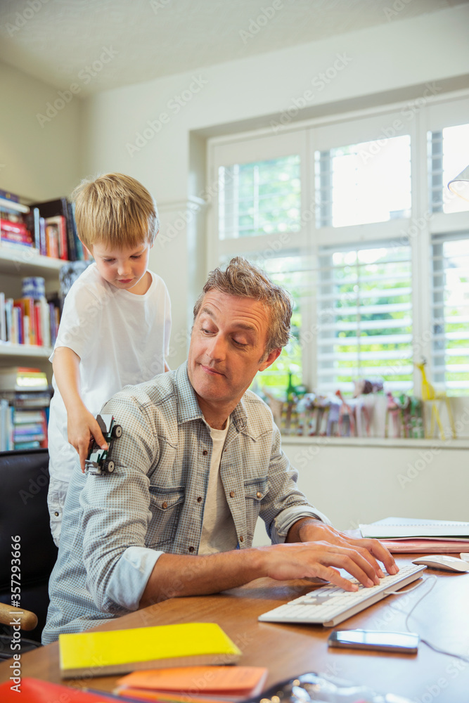 Boy distracting father at work in home office Boy distracting father at work in home office