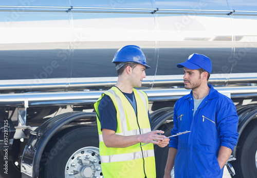 Workers with clipboard talking next to stainless steel milk tanker photo