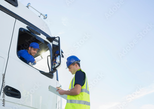 Worker with clipboard talking to truck driver photo
