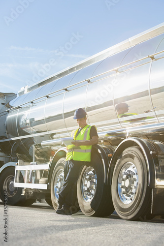 Worker with clipboard leaning on stainless steel milk tanker photo