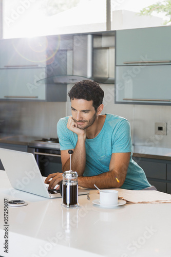 Man drinking coffee and using laptop in kitchen