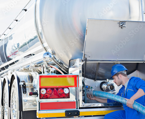 Worker attaching hose to back of stainless steel milk tanker