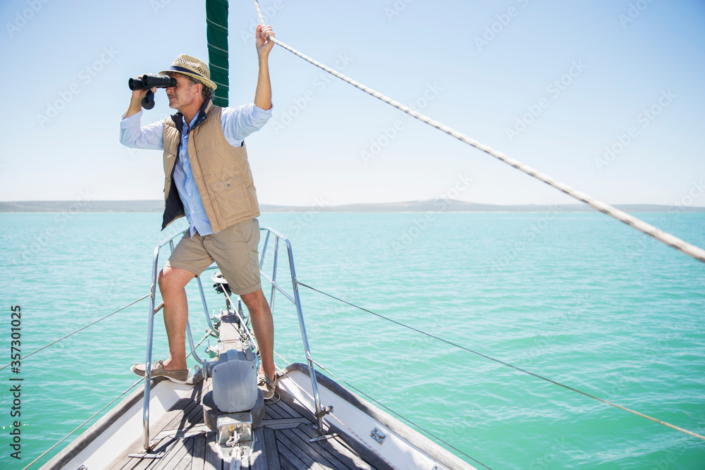 Older man looking out binoculars on edge of boat 