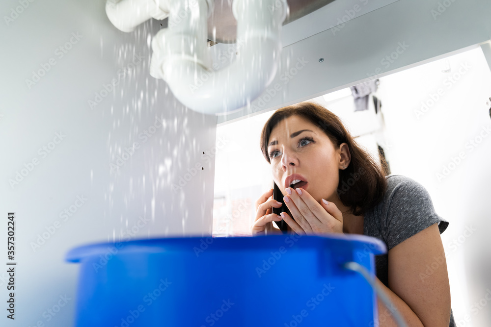 Women Doing Emergency Plumber Phone Call In Kitchen Women Doing Emergency Plumber Phone Call In Kitchen