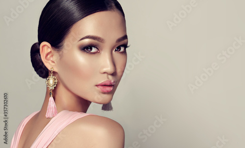 Asian model  fashion girl  with tassel earrings and  pink dress.  Oriental girl model, cosmetics, cosmetology and fashion.