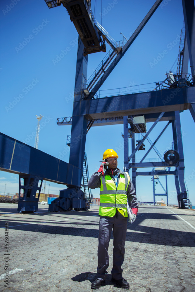 Worker talking on cell phone near cargo crane