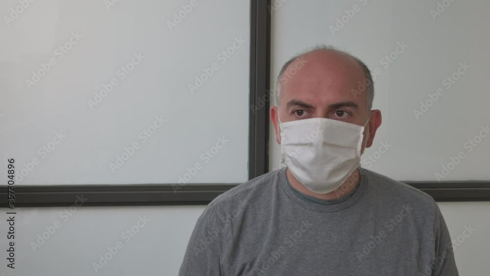 A middle-aged Caucasian man wears a white mask to protect himself from the coronavirus, suffers his pensive gaze. A middle-aged Caucasian man wears a white mask to protect himself from the coronavirus, suffers his pensive gaze.